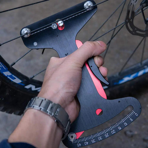 Hand holding a Bike Spoke Tension Meter With Caliper Aluminum Alloy Spoke Gauge For Accurate Tension Readings on a wheel