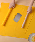 Hands rolling dough on yellow silicone baking mat with pastry cutter and bowl of eggs