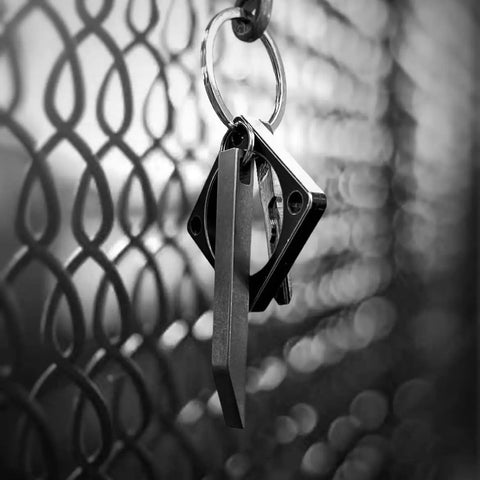 Beefy Heavy Duty Keychain Pry Bar For Everyday Carry hanging on a metal fence, stainless steel minimalist EDC multitool close-up.
