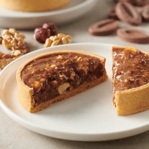 Hazelnut tart on a plate with walnuts and Creamy Milk Chocolate Feves For Baking 40 Percent Cacao No Fuss Melt And Temper Vanilla Malt.