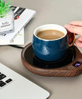 Keep Your Daily Drip Stayin Toasty With This Electric Coffee Mug Warmer Featuring Three Custom Temperature Levels Four Hour Auto Shut Off And Compact Desk Base For Zero Cold Sip Regrets. Blue ceramic mug on wooden electric warmer next to a laptop.