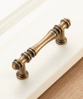 Close-up of a 3-inch antique brass cabinet pull on white panel, from 30 Pack 3 Inch Antique Brass Cabinet Pulls Set For Kitchen Cabinets, Drawers, Dressers And Cupboards, Vintage Brass Cabinet Handles Hardware With Free 25mm And 38mm Screws, Durable Solid Metal, Easy DIY Upgrade.