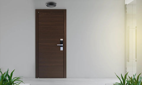 Lit LED Emergency Light With Manual Testing, 220 Lumens, Black, mounted above a dark wooden door in a commercial hallway