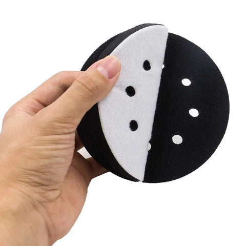 Hand holding Five Pack 5 Inch Soft Density Interface Pads with Eight Hole Design and Hook and Loop Backing, showing sponge cushion.