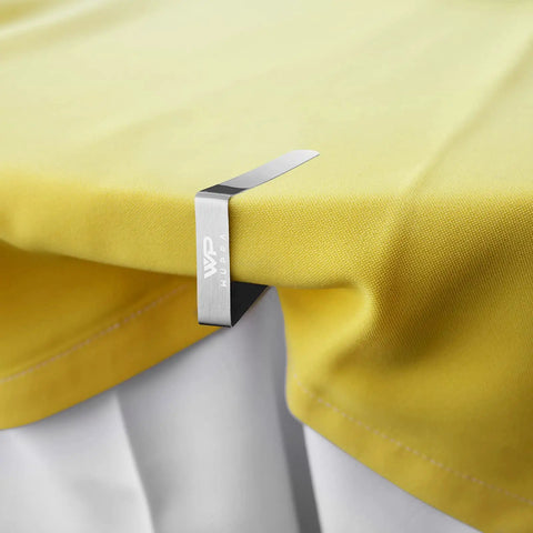 Close-up of 12 Pack Tablecloth Clips For Outdoor Tables, Stainless Steel Heavy Duty Table Cloth Holders, securing yellow fabric to table.