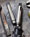 Two steel Morse taper adapter sleeves with drill chuck and knurled collar on workshop bench.
