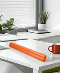 Orange tube on white desk in office setting with plants and books, not showing Adjustable Telescoping Poster Tube 52 to 95 cm for Posters.