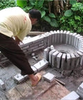 Man assembling a small hydrogenerator installation with bricks outdoors, featuring a circular die-cast aluminum alloy case base.