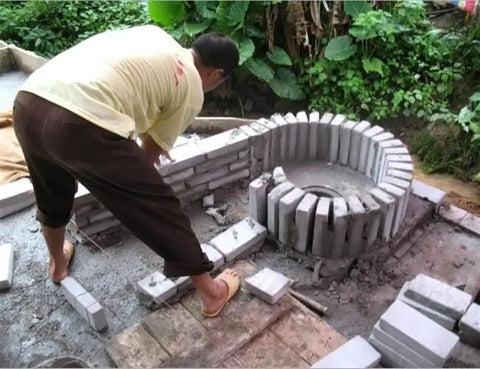 Man assembling a small hydrogenerator installation with bricks outdoors, featuring a circular die-cast aluminum alloy case base.