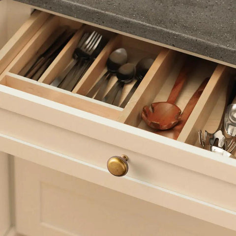 Open drawer with utensils showing antique brass kitchen cabinet knob with beaded edge, secure grip design on light wood dresser.