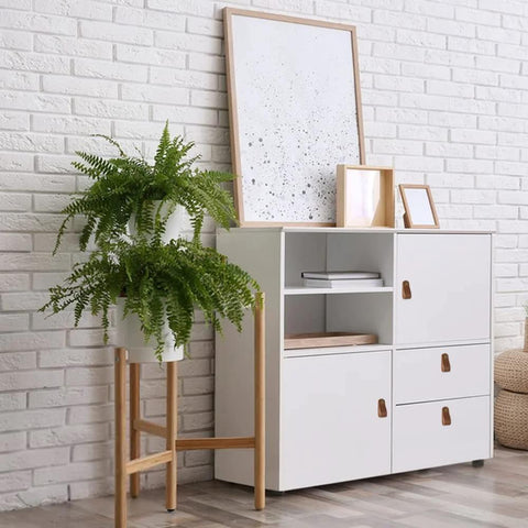 White cabinet with Six Piece Leather Drawer Pulls Set In Brown With Gold Rivet Screws, 4.72 Inch Soft Handles, near a plant.