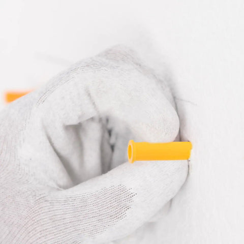 Inserting Heavy Duty Yellow Self Drilling Wall Expansion Anchor Kit into hollow wall, close-up on hand.