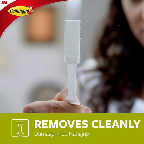 Person holding a medium white Damage Free Picture Hanging Strip For Walls No Tools Needed Medium And Large White Mounts For Quick Decor