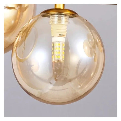 Close-up of glass ball pendant light in a modern chandelier for dining room, featuring LED bulb and gold accents.