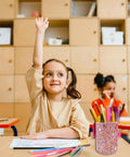 Glitter Pink Desk Pen Holder And Makeup Brush Organizer Cup on a classroom desk with children studying in the background.