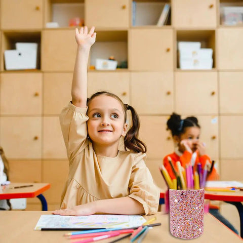 Glitter Pink Desk Pen Holder And Makeup Brush Organizer Cup on a classroom desk with children studying in the background.