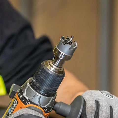 Close-up of a drill using Heavy Duty Hole Cutter Kit With Carbide Cutters And Two Pilot Bits In Rust Proof Molded Plastic Case Eight Piece Workhorse Set For Fast Precise Holes In Stainless Steel Mild Steel Iron Copper And Brass Up To Three Sixteenth Inch Thick on metal sheet.
