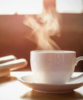 Steaming white ceramic coffee cup on saucer with blurred background
