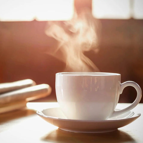 Steaming white ceramic coffee cup on saucer with blurred background