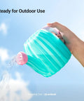 Hand holding a turquoise watering can outdoors, ready for outdoor use with water pouring from the spout.