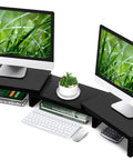 Dual Monitor Stand Riser For Desk Setup With 3 Shelf Adjustable Length And Tilt Extra Long Multifunctional Wood Stand Fits Computer Laptop TV Up To 43 Inches Black, holding two monitors and a plant.