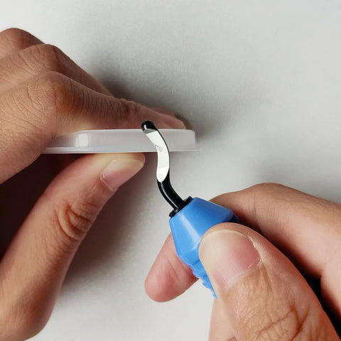 Close-up of blue-handled deburring tool with curved blade, working on a white circular edge