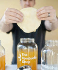 Person holding SCOBY over jars containing 100 Percent Organic SCOBY Kombucha Starter Kit For Home Brew Sessions With Live Culture