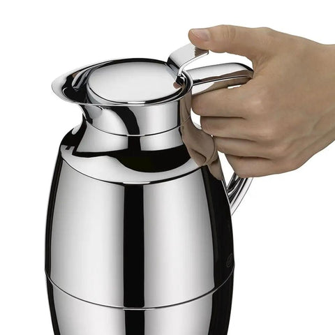 Hand holding One Hand Pour Glass Vacuum Carafe 1 Liter Capacity With Chrome Plated Brass Thermal Dispenser Keeps Coffee Hot 12 Hours Cold 24 Hours Easy Screw Stopper For Spill Free Pour Metallic Finish