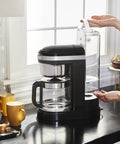 Side view of a 12 Cup Drip Coffee Maker With Spiral Showerhead And Programmable Keep Warm Plate For Rich Consistent Brews Every Time Onyx Black KCM1209 No Fuss Programmable Timer Auto Shutoff Large Water Reservoir For Busy Mornings on a kitchen counter