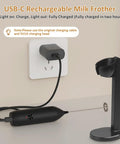 Rechargeable USB Type C Milk Frother Handheld With Stand shown charging with USB-C cable, black color, stand beside it.