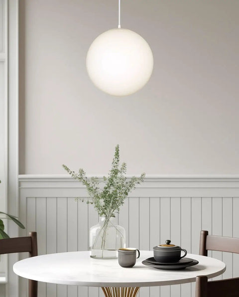 Mid Century Modern Globe Pendant Light With Frosted Glass Orb, White Finish above a dining table with plants.