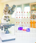 Chill Out Your Lab Setup With This Sleek White Metal Test Tube Drying Rack next to a microscope on a lab table.
