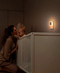 Sujeet night light; white plug-in wall LED emitting warm white glow above a baby's crib.