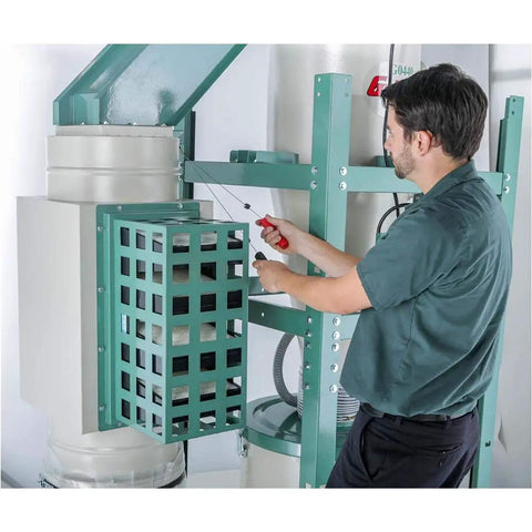 Man adjusting the filter of a 2 Horsepower Dual Filtration HEPA Cyclone Dust Collector in a workshop setting.
