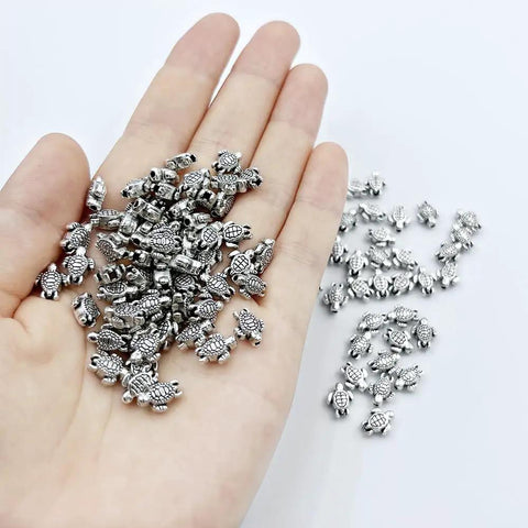 Hand holding 100 Pcs Dope Tiny Turtle Beads Antique Silver 0.9x0.7cm Mini Turtle Shaped Metal Beads For Crafts Jewelry Making