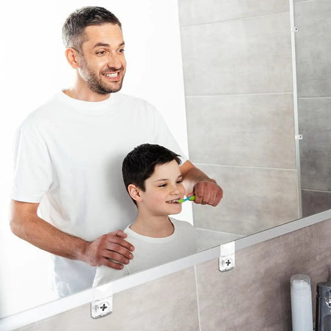 A father helps his son brush teeth in front of a mirror secured with Pretty Slick Mirror Holder Clips With Screws For Effortless Frame And Cabinet Door Mounting Includes Thirty Clear Plastic Hanging Hardware Sets For Quick Wall Glass Install Jobs.