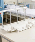 Adjustable Bed Rail Brackets For Home Beds on table in care setting, white aluminum material, drop-down safety rails visible