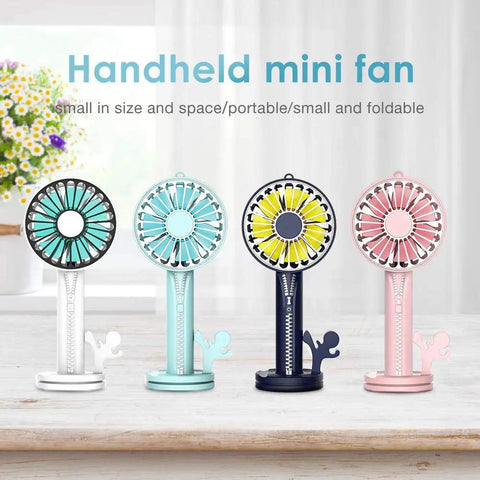 Four colorful handheld mini fans on a table, showing black, teal, navy, and pink designs, with visible buttons and stands.