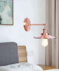 Heavy Duty Adjustable Wall Sconce Featuring Straight Up Industrial Design Foolproof Mounting E27 Base Solid Bronze Glow Ideal For Reading Lounge Bath Or Guest Room In Rich Red Tone mounted beside a bed with a warm light.