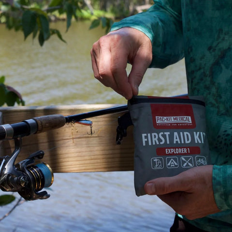 Pac-Kit Medical Explorer 1 First Aid Kit in gray watertight pouch, being opened on a boat with fishing rod.