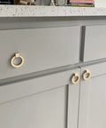 6 Pcs Brushed Brass Cabinet Ring Pulls Set In Zinc Alloy With Durable Single Hole Design installed on gray kitchen cabinets.