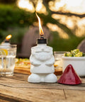 Close-up of a white gnome table torch with a flame and red snuffer, part of a Two Pack Gnome Table Torches For Outdoor Patio And Backyard.