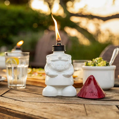 Close-up of a white gnome table torch with a flame and red snuffer, part of a Two Pack Gnome Table Torches For Outdoor Patio And Backyard.