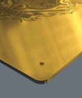 Close-up of a gold metal plate with decorative design and a small hole near the edge on a gray background.