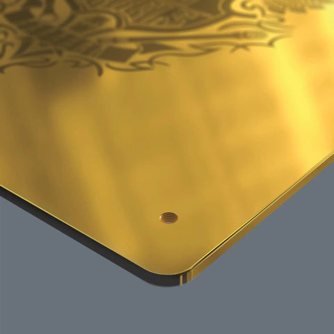 Close-up of a gold metal plate with decorative design and a small hole near the edge on a gray background.