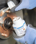 WEICON Copper Paste bottle (copper anti-seize) applied to a rusted wheel hub assembly by gloved hands