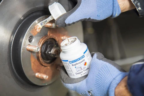 WEICON Copper Paste bottle (copper anti-seize) applied to a rusted wheel hub assembly by gloved hands