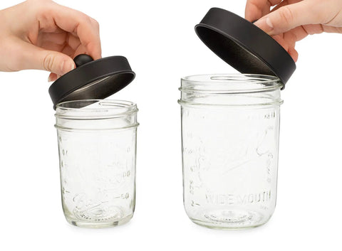 Hands holding apothecary lid storage set with Ball mason jars, 16 oz wide-mouth and 8 oz regular-mouth, black finish.