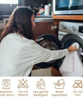 Woman loading white cotton towel into washing machine with laundry care symbols below.