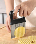 Front view of a stainless steel crinkle cutter with a black handle slicing ridged potato fries.